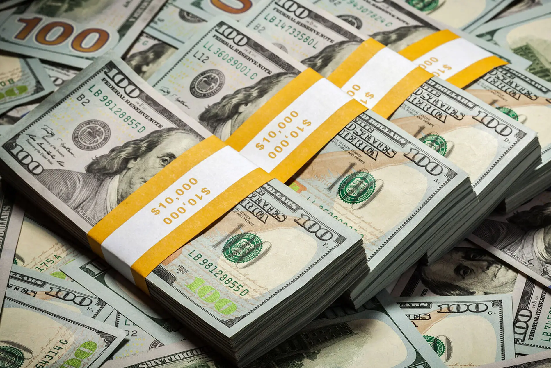 Stacks of $100 U.S. dollar bills with yellow bands labelled $10,000, surrounded by loose bills.